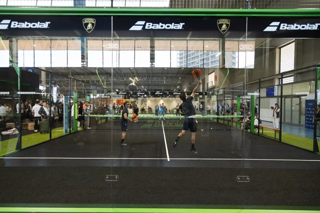 Babolat et Lamborghini dévoilent les nouvelles BL.002 Bronze et Orange à Barcelone À l’occasion du Padel World Summit de Barcelone, Babolat a présenté les deux nouvelles déclinaisons de sa raquette premium BL.002, développée en collaboration avec Automobili Lamborghini. Les versions Bronze et Orange viennent enrichir une collection déjà très identifiée dans l’univers du padel haut de gamme. Un lancement loin d’être anodin pour la marque française, qui continue d’ancrer une partie stratégique de son développement padel à Barcelone, là même où la BL.002 est fabriquée au sein du Babolat Padel Studio. Barcelone, centre névralgique du projet Babolat padel Pour cette présentation, Babolat a choisi le Padel World Summit, devenu ces dernières années le principal rendez-vous international de l’industrie du padel. Fabricants, distributeurs, clubs, fédérations et médias spécialisés s’y retrouvent chaque année, faisant de l’événement une vitrine idéale pour dévoiler les nouveaux projets de la marque. La journée a débuté dans le showroom de Lamborghini Barcelona, où les invités ont découvert les nouvelles versions de la BL.002 entourées des supercars de la marque italienne. Plus qu’un simple changement esthétique, Babolat explique avoir directement puisé dans l’univers visuel de Lamborghini pour imaginer ces nouvelles finitions. Les coloris Bronze et Orange reprennent ainsi plusieurs codes emblématiques de la marque automobile italienne, dans une logique de continuité entre luxe, performance et design. Une expérience pensée autour du premium L’événement s’est ensuite poursuivi au Padel World Summit, où la société Greenset avait conçu une piste exclusive spécialement imaginée pour cette activation. Le terrain intégrait plusieurs technologies récentes développées par l’entreprise espagnole. Fernando Cánovas Llopis, co-CEO de Greenset, est revenu sur ce projet : « Créer une piste exclusive avec l’une des marques les plus iconiques du monde automobile nous a demandé énormément de travail en ingénierie, innovation et design. » Avant d’ajouter : « Une fois le résultat final terminé, nous pensons que c’est une piste qui ne laissera aucun joueur indifférent. » Du showroom Lamborghini jusqu’à la piste installée au salon, toute la journée avait été pensée comme une expérience de marque complète, mêlant esthétique, technologie et performance. Une stratégie premium de plus en plus affirmée Avec cette collaboration autour de la BL.002, Babolat continue surtout d’affirmer son positionnement premium dans l’univers du padel. La marque française, historiquement connue pour avoir inventé les premiers cordages de tennis en 1875, multiplie depuis plusieurs années les partenariats prestigieux autour du sport et du lifestyle. Dans son portefeuille figurent notamment Juan Lebrón, Rafael Nadal ou encore Carlos Alcaraz, mais aussi des collaborations avec Wimbledon, Michelin, Club Med et désormais Lamborghini. La BL.002 apparaît aujourd’hui comme l’un des produits les plus représentatifs de cette stratégie : une raquette mêlant image haut de gamme, innovation technologique et univers automobile. Les nouvelles versions Bronze et Orange seront disponibles à partir du 5 juin 2026 dans une sélection de magasins ainsi que sur le site officiel de Babolat