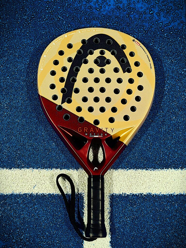 Close-up of a yellow perforated paddle with a red grip on a blue court surface.