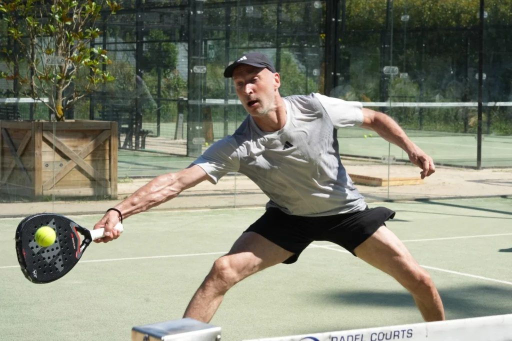 WhatsApp Image 2026-06-29 at 163147 | Padel Magazine Man in a cap lunges to hit a padel ball with a paddle on an outdoor court.