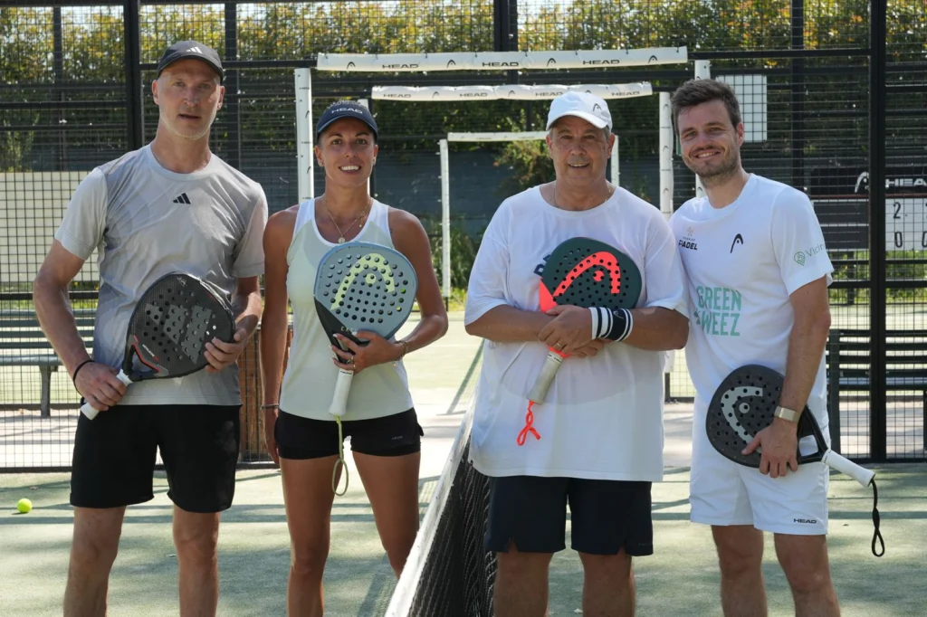 WhatsApp Image 2026-06-29 at 163220 | Padel Magazine Four people stand on a padel court behind a net, each holding a perforated paddle and smiling at the camera.