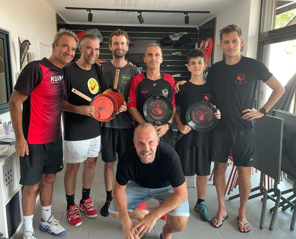 picture | Padel Magazine Seven people in athletic gear pose together indoors, holding red-and-black circular awards and smiling at the camera.