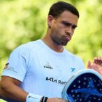 Man in a light blue shirt holds a padel racket outdoors, looking focused.