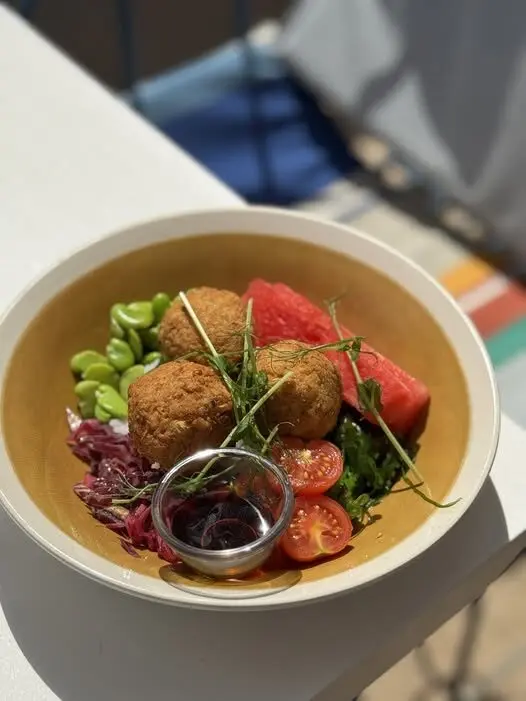 Kulhollinen falafeleja, vihreitä, edamame-papuja, kirsikkatomaatteja, vesimelonikuutio ja pieni kuppi dippikastiketta vierekkäin.