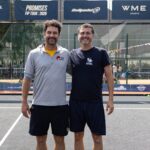 3V3A2014 | Padel Magazine Two men stand together on a padel court, smiling, with banners for the International Padel Federation in the background.