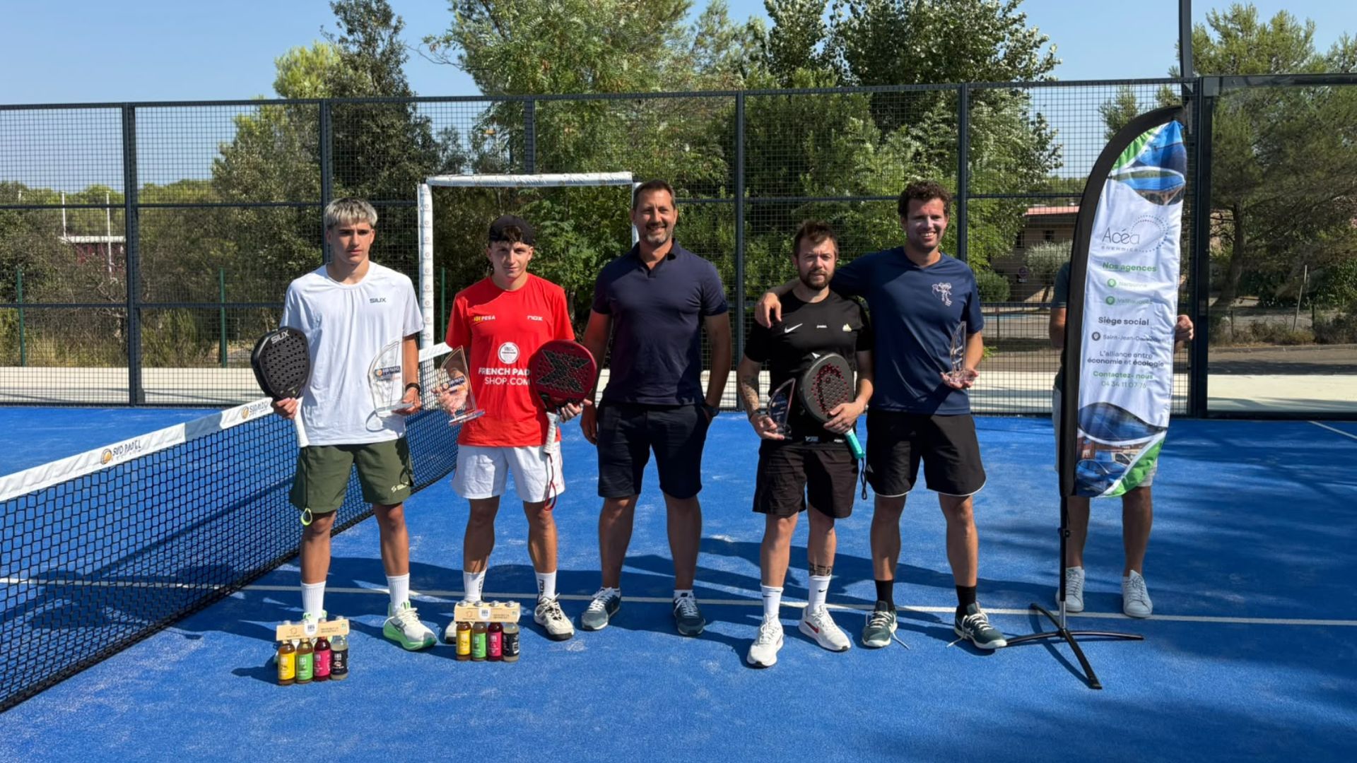 Bernard et Rubio confirment leur statut et soffrent le titre au P1000 Sud Padel Bel Air | Padel Magazine Six men pose with rackets and trophies on a bright blue padel court after a match, drinks lined up in front, a banner nearby.