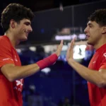 Coello chambre Tapia avant la finale de la coupe du monde et lEspagne lui donne raison | Padel Magazine Two male athletes in red jerseys high-fiving in a dimly lit sports arena.