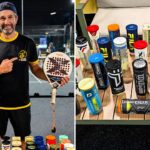 Man in black and yellow shirt holding a padel paddle on an indoor court, smiling at the camera.