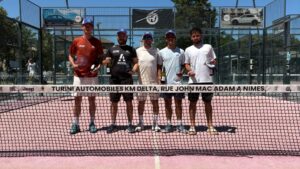 Five men in blue caps stand side by side on a pink outdoor court, holding trophies and bottles after a match.