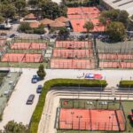 P2000 WinWin Padel Cabriès les qualifiés sont connus place au tableau final | Padel Magazine Aerial view of a sports complex with many red clay tennis courts fenced in, surrounded by trees and a parking lot.