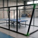PING PONG PADEL 2 | Padel Magazine Indoor gym featuring a blue table tennis table inside a glass-walled enclosure, with people in the background.