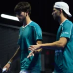 Pretoria P1 Boronad et Fonteny passent tout près du gros coup face à Fernandez et Vilariño | Padel Magazine Two male padel players in teal jerseys greet each other at the net, one wearing a white cap backward, indoors.