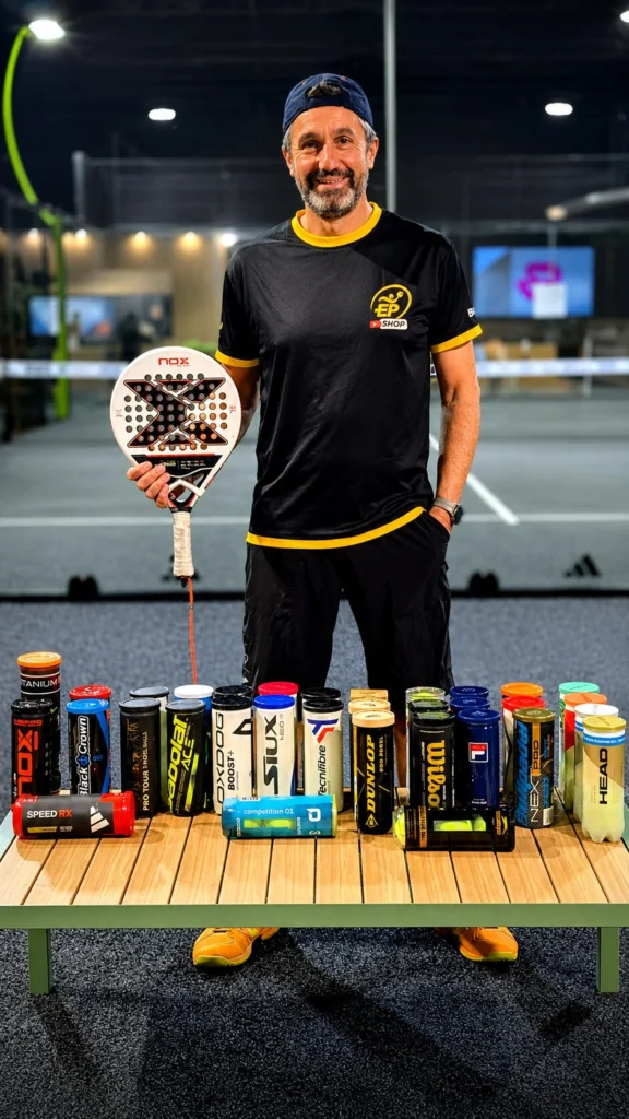 Un uomo in abbigliamento sportivo è in piedi dietro un tavolo pieno di lattine colorate di energy drink, mentre impugna una racchetta da padel in un campo da padel.