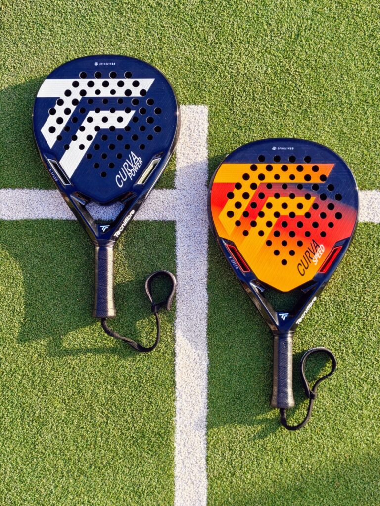 oplus_2162736 | Padel Magazine Two padel rackets resting on a green court near a white line, one blue and one orange/blue design.