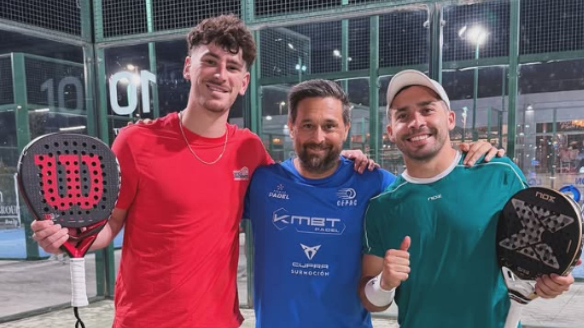 Three men posing together on a padel court, each holding a paddle and smiling at the camera after a game.