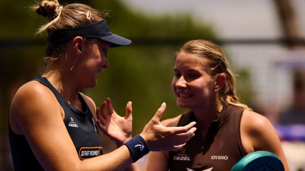 Two female padel players celebrate with a high-five during a sunny outdoor match.