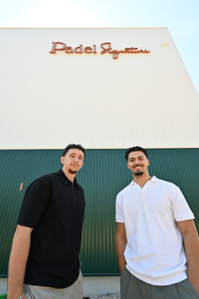 Padel Signature : un nouveau club premium ouvrira ses portes à Montauban en août 2026 | Padel Magazine Two men stand in front of a white building with a red'Padel Signature' sign and a green corrugated wall behind them.