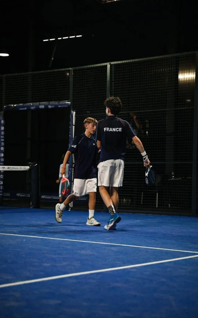image | Padel Magazine Two male tennis players in navy shirts and white shorts high-five on a blue indoor court, one with 'France' on his back and both holding rackets.