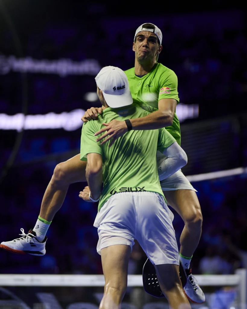 Due tennisti con indosso magliette verde lime identiche festeggiano con un abbraccio a mezz'aria su un campo da tennis durante una partita di doppio, con le braccia intorno l'uno all'altro.