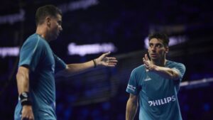 Zwei männliche Padelspieler in blauen Hemden klatschen sich auf einem schwach beleuchteten Platz ab.