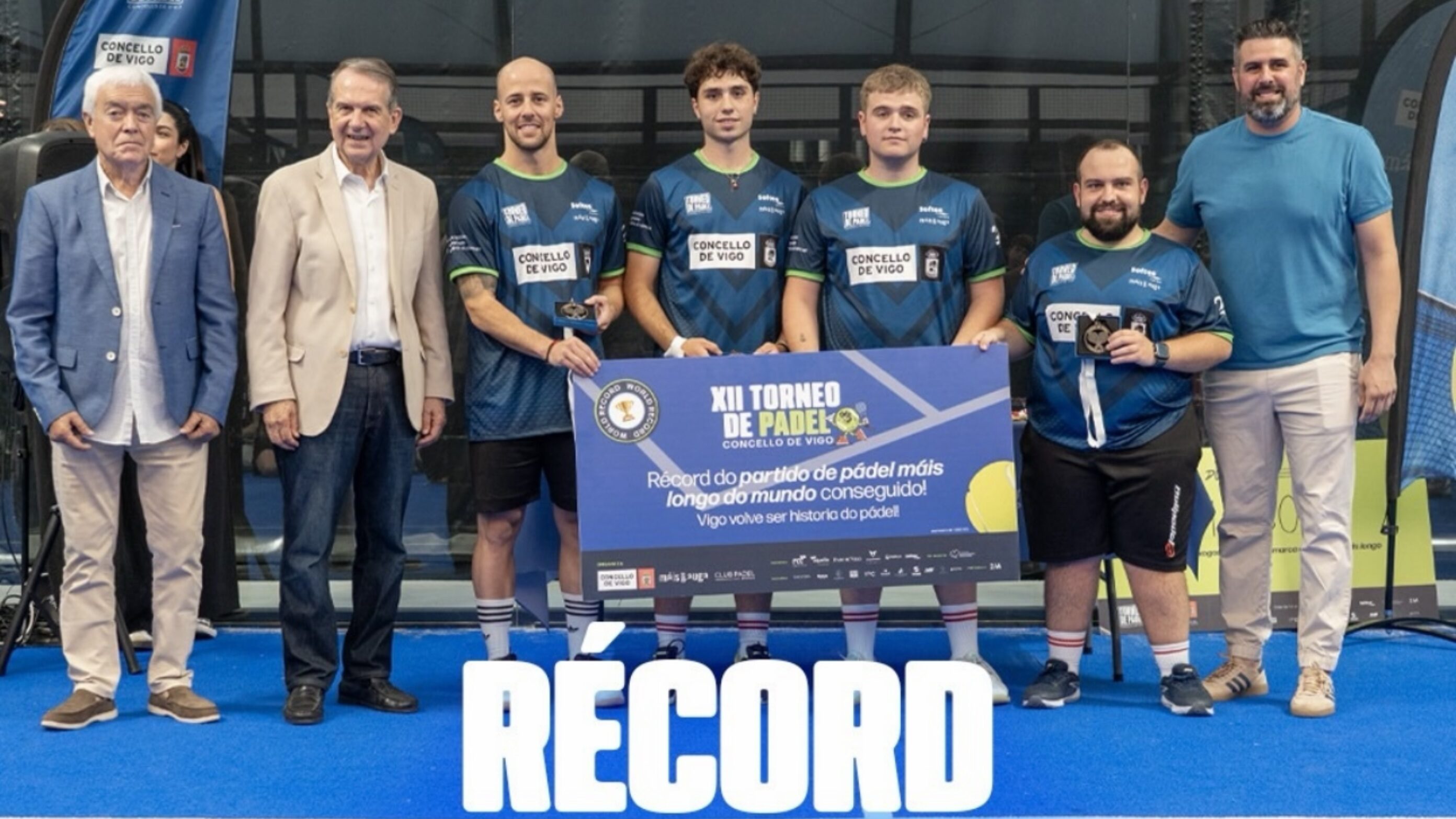 Group of men and young players pose with trophies at a paddle tennis event, wearing blue jerseys with Concello de Vigo logos.