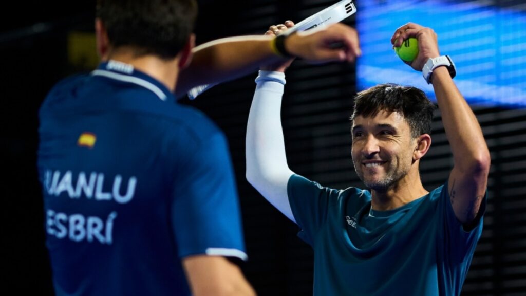 Two athletes celebrate a win by high-fiving; one man in teal shirt smiles as he raises a tennis ball in his right hand. Contrasty background stadium lights behind.