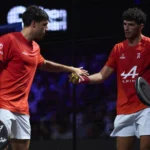 Two male floorball players in red shirts high-fiving on an indoor court.
