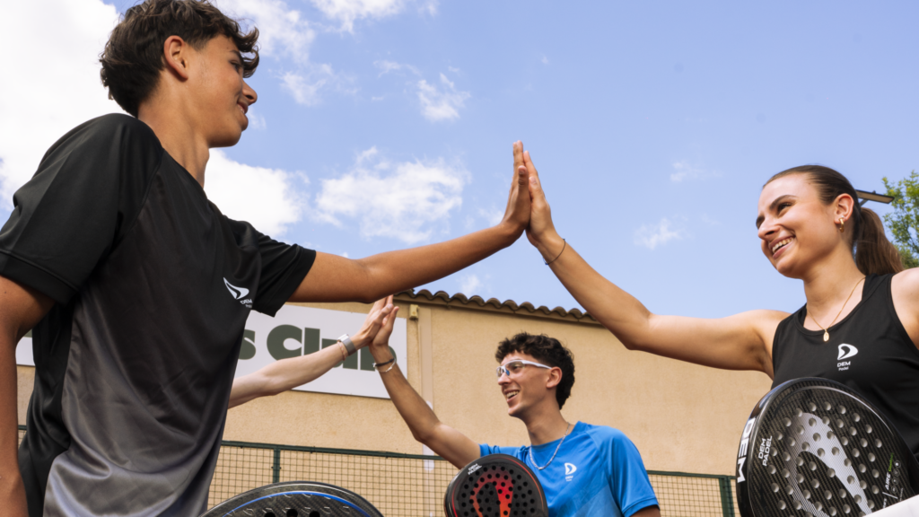 Group of young players on an outdoor padel court high-fiving in celebration, paddles in hand