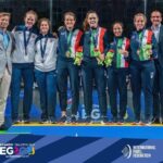 Eight athletes stand on a podium with medals, flanked by two coaches, at a padel event.