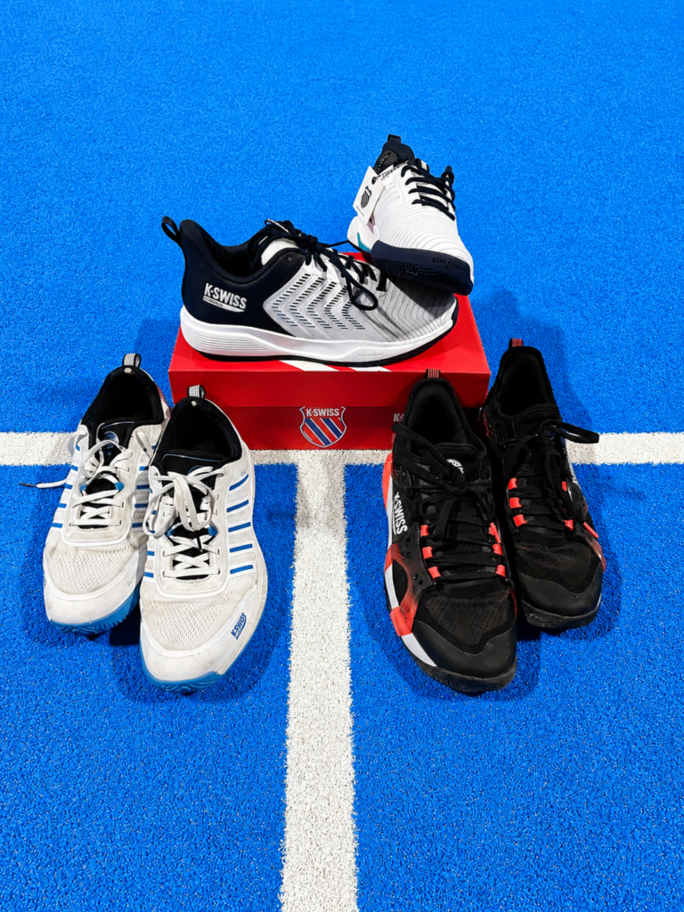 Famille KSwiss | Padel Magazine Several running shoes arranged around a red K-Swiss box on a bright blue track with a white line across the ground.