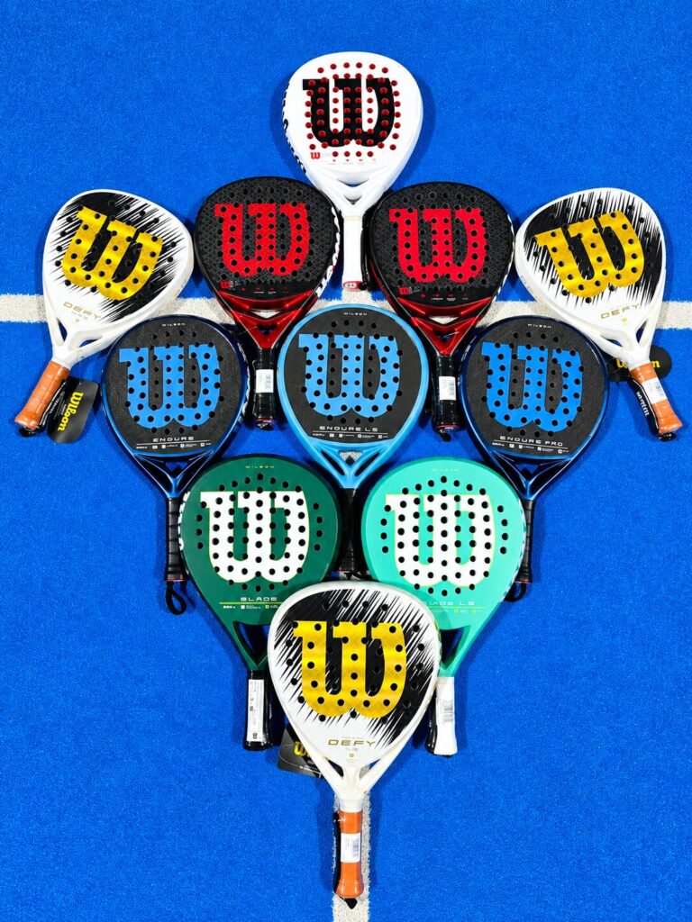 Family Wilson | Padel Magazine A heart-shaped arrangement ofWilson tennis rackets in various colors on a blue tennis court surface on white line accents.