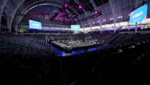 Indoor arena with a central competition court and surrounding empty seats, large screens display London PT banners under purple stage lights.