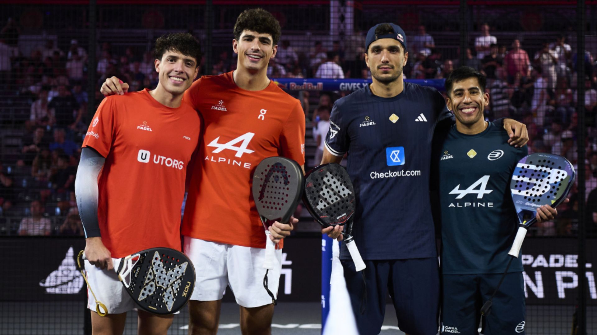 Tapia Coello vs Chingotto Galán une rivalité spectaculaire mais devenue trop répétitive | Padel Magazine Four male padel players stand side by side on court, holding paddles, smiling as spectators watch in the background.