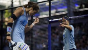 Two female players in light blue jerseys celebrate on a court, one pointing toward the camera as the other clenches a fist in the background.