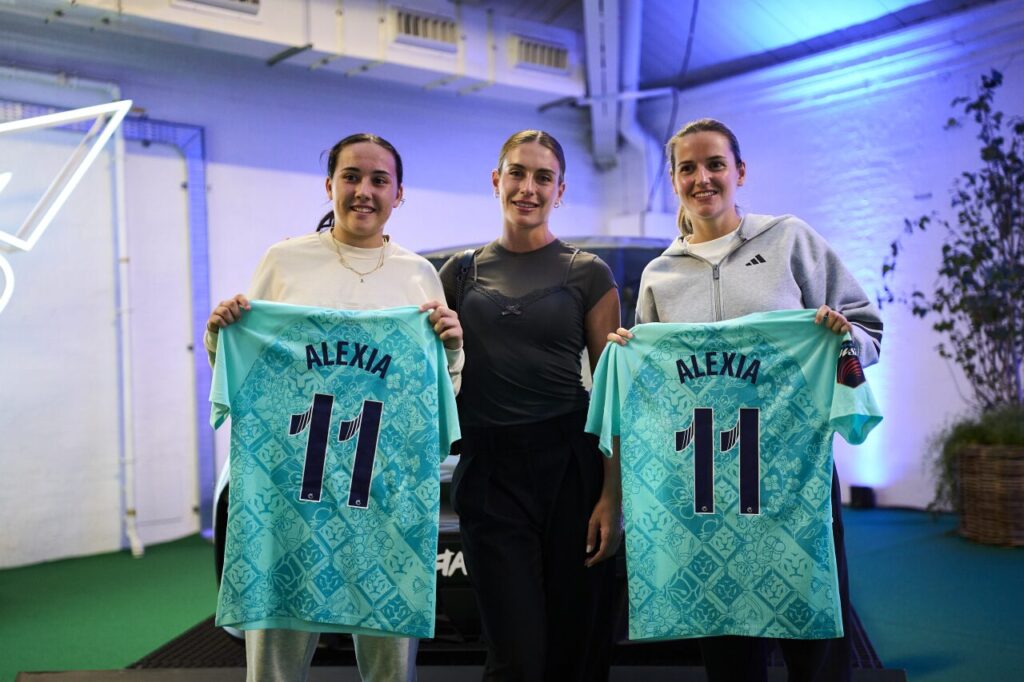 image | Padel Magazine Three women stand smiling in a gym, two holding turquoise soccer jerseys reading ALEXIA and 11 on both backs. central person wearing black.
