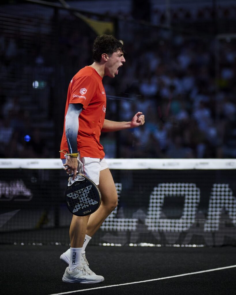image | Padel Magazine Male padel player in an orange jersey celebrates on court, racket in hand, during a match.