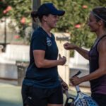 P1500 La Ciotat – Les trois premières têtes de série au rendez-vous, Lefevre / Alquier créent la surprise | Padel Magazine Two women in athletic wear share a fist bump outdoors near a sports court, smiling.