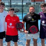 Four male padel players pose together on a blue court, each holding a paddle and smiling at the camera.