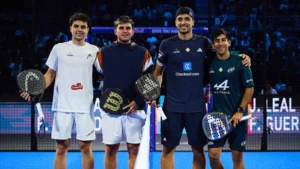 Four male padel players stand together on a blue court, holding their paddles and smiling after a match.