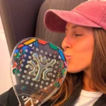 Pretoria redistribue les cartes : Galán, Triay et Chingotto grimpent au classement des joueurs les plus titrés | Padel Magazine Close-up of a young woman wearing a pink cap kissing a colorful padel racket covered in geometric patterns and dots.