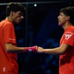 Tapia et Coello arrêtés à 27 : une série historique qui redéfinit le padel moderne | Padel Magazine Two male athletes in orange jerseys shake hands on an indoor court after a match.