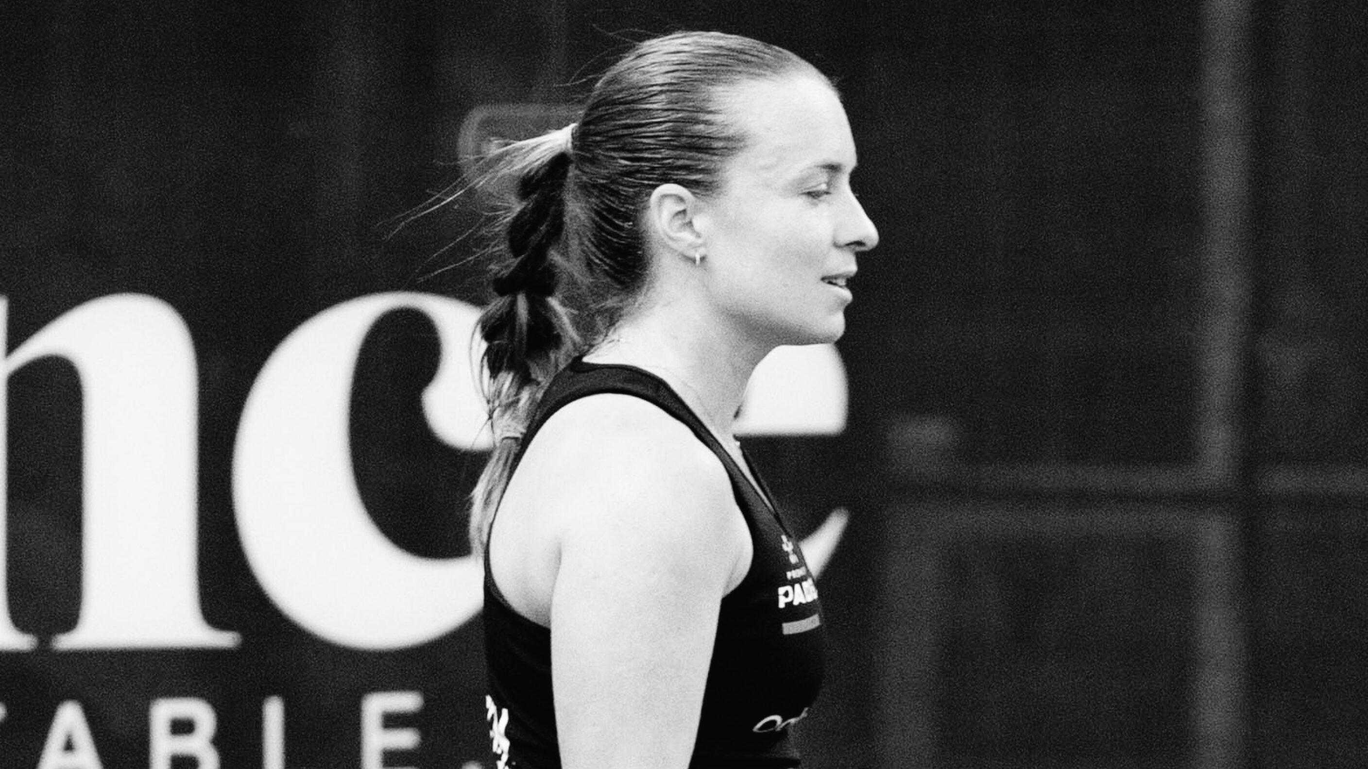 P1 de Londres – Carla Touly s'arrête aux portes du tableau principal, Collombon et Leygue prennent le relais | Padel Magazine Side profile of a female athlete with a braided ponytail wearing a black tank top at a competition, in black-and-white.