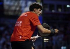 Male athlete in an orange shirt grips a squash racket during a match, focused on the play.